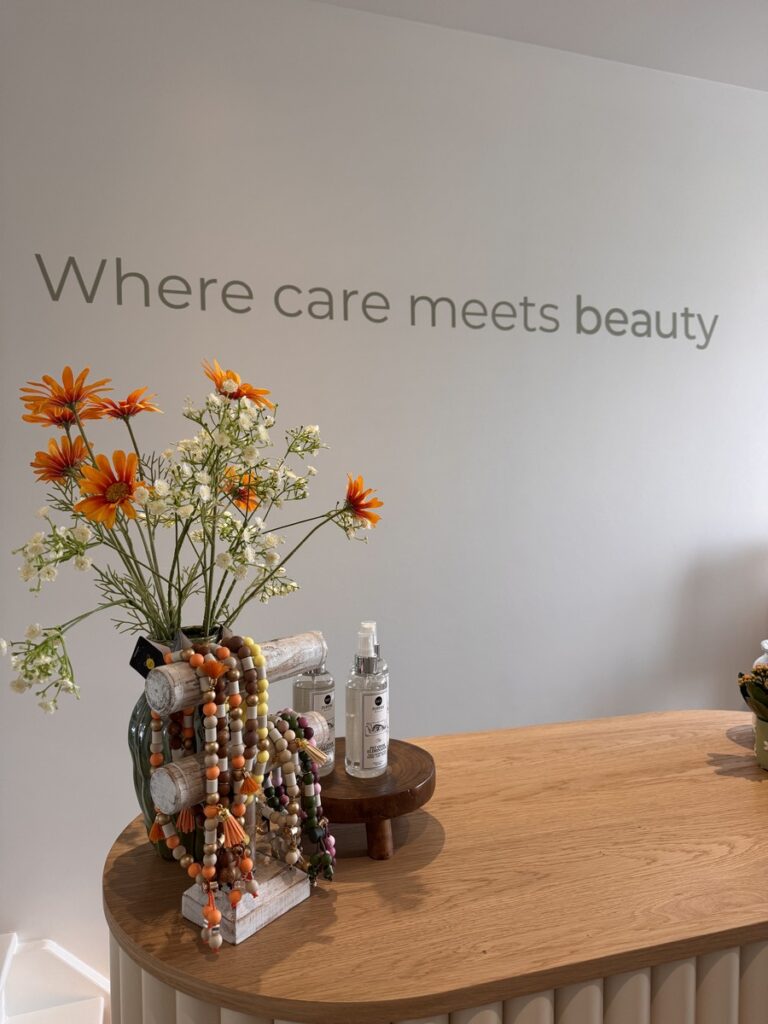 Floral arrangement and beauty products on a wooden counter under the wall slogan 'Where care meets beauty'.