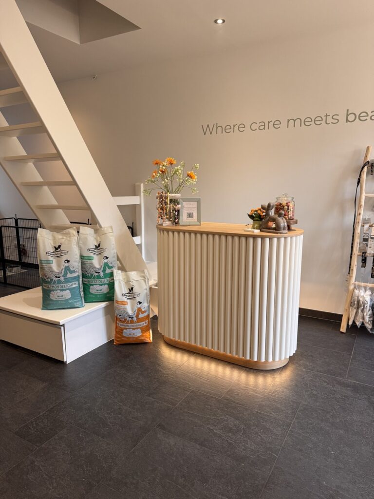 Reception desk with vertical white slats, small flower arrangement, and bags of pet food nearby under a staircase.